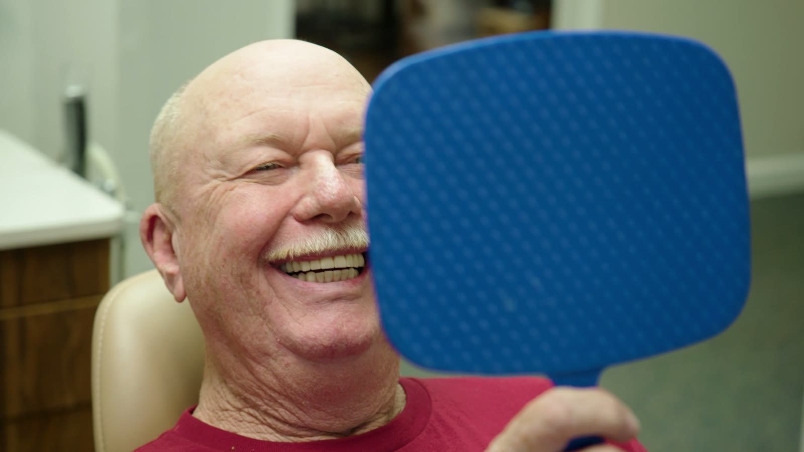 A real Tim Rauch DDS patient laughing at the mirror after their full-arch implant restoration